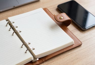 A close-up shot of a modern leather planner and a charcoal smartphone on a clean wooden desk, symbolizing professional organization and content management.