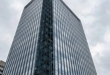 An architectural exterior shot of a sleek, glass-walled corporate building in Brazil, reflecting a light gray sky. The style is professional and modern, symbolizing corporate law and commercial strength. Sharp angles and professional lighting.