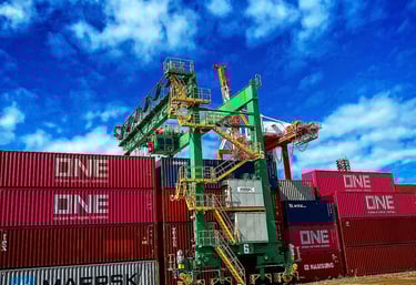 A green industrial gantry crane stacking pink ONE and silver Maersk shipping containers at a busy port.