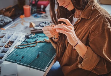 Creadora de joyería elaborando un collar hecho a mano con cuentas en un espacio de trabajo creativo.