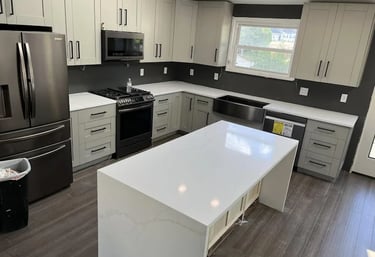 A newly renovated modern kitchen with light gray cabinets, white quartz countertops, stainless steel appliances, and a