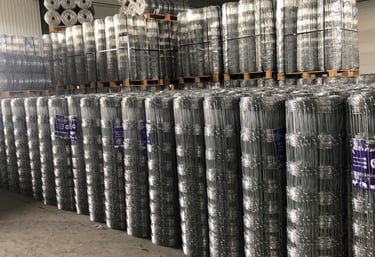 Stacks of galvanized cattle fence wire rolls neatly arranged in a warehouse, showing the bulk storage of livestock fencing pr