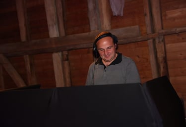 Professional DJ wearing headphones and mixing music at an event with a rustic wooden wall background.