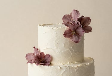 A stunning, minimalist cake design with white textured frosting and soft mauve floral accents, set against a warm cream background. Elegant studio photography.