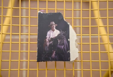 A torn vintage photo of a man in a straw hat with a dog resting on a yellow grid surface.