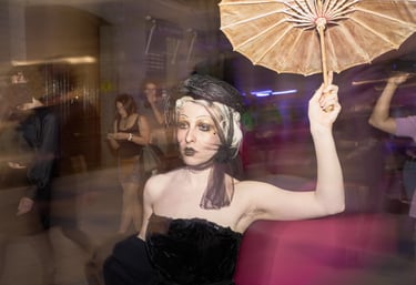Woman in vintage gothic costume with a black veil, gold makeup, and holding a tan parasol.
