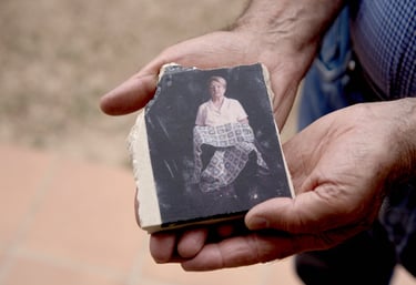 Hands holding a broken ceramic tile featuring a portrait of an elderly woman holding a blanket.