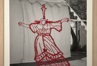 Framed black and white photo featuring red embroidery of a woman's dress onto a canvas tent.