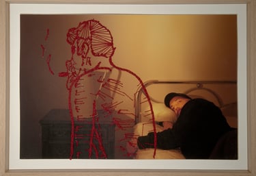 Red embroidery of a figure overlaying a photograph of a man lying in a metal bed frame.