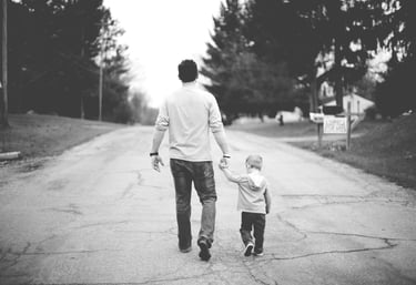 Black and white photo of a father and young son walking hand in hand down a quiet suburban street. 