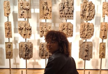 a woman sitting on a bench in front of a wall with a number of carvings