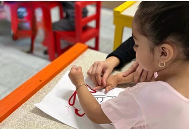 Niña en edad preescolar desarrollando la motricidad fina al pegar hilo rojo 