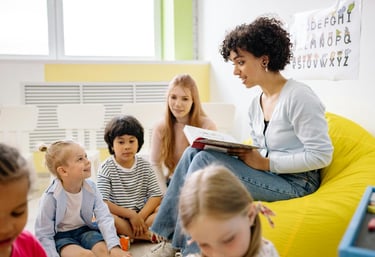 Maestra sonriente leyendo un libro de cuentos a niños en edad preescolar sentados en el suelo del au