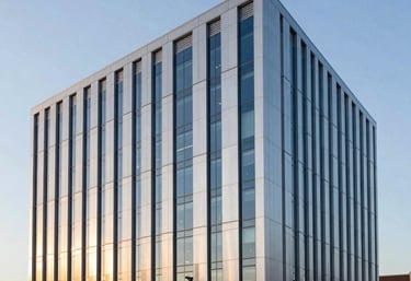 An architectural photography shot of a sleek, modern North American / US corporate headquarters at sunrise. The building features large silver panels and blue glass, reflecting a sense of stability and institutional trust.