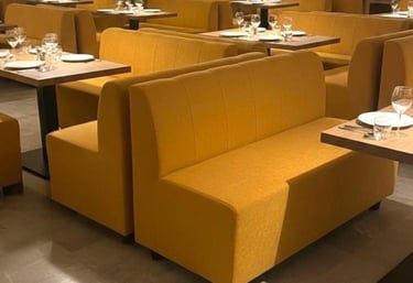 Modern restaurant interior featuring rows of mustard yellow upholstered booth seating and set dining tables.