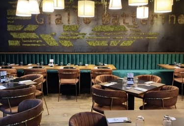 Modern restaurant interior featuring velvet chairs, green booths, and hanging plants with warm lighting.