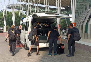 Lima orang laki-laki dewasa sedang menaikkan bagasi ke mobil Hiace warna putih.