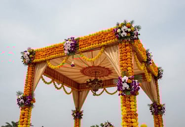 A vibrant photograph of a South Asian wedding mandap, exquisitely decorated with marigolds and orchids, set against a soft silver-gray sky in Jharkhand.