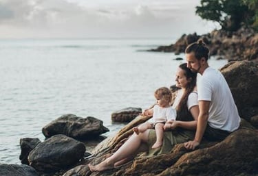 Una familia feliz con un niño pequeño sentada sobre rocas marinas en una playa