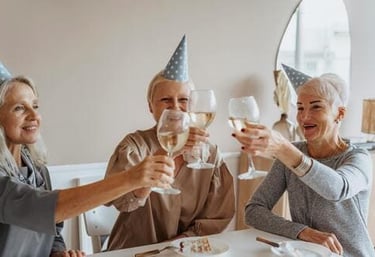 Tres mujeres mayores con sombreros de fiesta haciendo un brindis con vino en una celebración