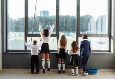 Estudiantes con uniformes escolares mirando por un gran ventanal hacia un patio de recreo