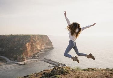 Una mujer feliz saltando en el aire en un acantilado pintoresco con vistas al océano al atardecer