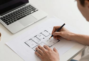 Close-up of hands sketching architectural plans with an orange pencil.