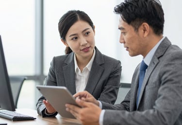 A professional man and woman in business attire discussing a commercial property portfolio over a tablet in a bright office. The vibe is professional and collaborative, with a modern aesthetic.