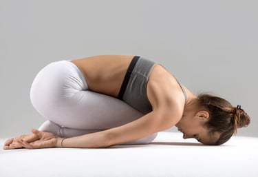 Una mujer con leggings blancos practicando Balasana o Postura del Niño para la relajación del yoga.