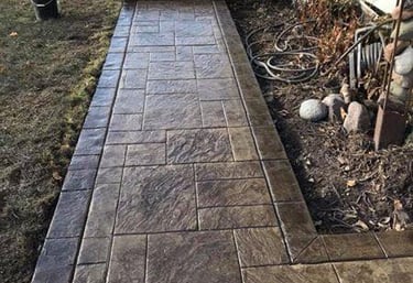 Custom dark brown stamped concrete walkway with a textured slate pattern leading to a home entrance.