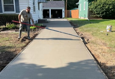 Professional contractor finishing a fresh concrete driveway installation with broom finish.