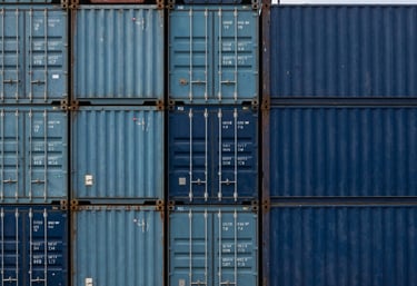 A top-down view of a stack of clean, modern shipping containers in shades of steel blue and navy blue.