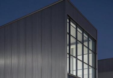 Clean, minimalist architectural photography of a modern sustainable industrial building facade, carbon gray steel and glass, deep navy twilight sky.