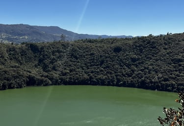 Panoramic view of Lake Guatavita, a green volcanic crater lake surrounded by lush forest in Colombia.