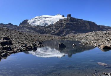 Snow-capped mountain peak reflected in a clear alpine glacial lake under a bright blue sky.