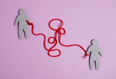 Two paper human figures connected by a tangled red string representing complex emotional connections.