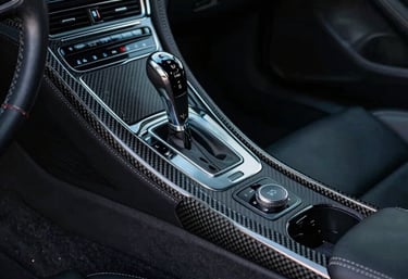 Interior of a luxury sports car featuring carbon fiber trim, black leather with silver stitching, and soft atmospheric blue lighting, International / Global.