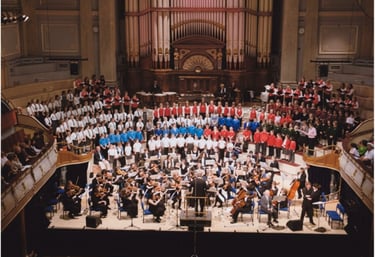A large youth choir and symphony orchestra perform a concert on stage in Huddersfield Town Hall.