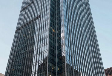 An abstract architectural photograph of a modern skyscraper in a North American city, looking up at the glass facade under a clear sky.