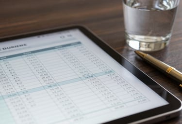 A macro shot of a financial spreadsheet on a tablet next to a glass of water and a gold pen in a quiet corporate setting.