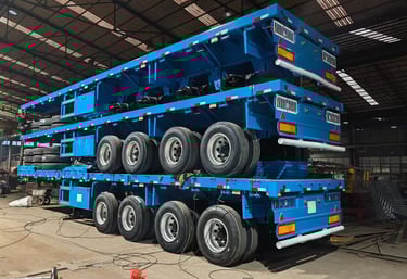 Three blue heavy-duty flatbed semi-trailers stacked for transport in our manufacturing warehouse.