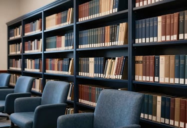 Photography of a high-end corporate library with dark navy shelves and slate blue chairs, representing precision, wisdom, and the depth of professional research in a global business context.
