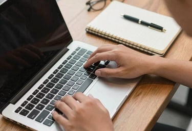 A top-down view of a person using a laptop and a notebook in a modern cafe in Indonesia, focus on hands and technology, clean and warm atmosphere.