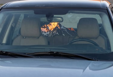 A stunning photograph of a luxury SUV's windshield perfectly reflecting a sharp, clear North American mountain sunrise, illustrating the theme of clarity and high-quality glass.