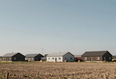 A wide-angle view of an orderly farmstead under a clear blue-grey sky. The buildings are well-maintained, representing modern quality and reliability. Palette: #F4F0E7, #6F624C.