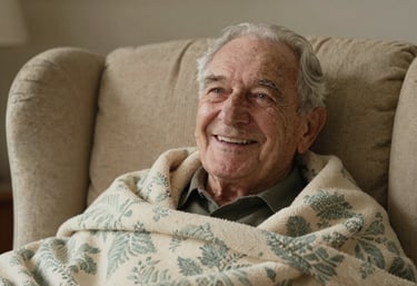 A close-up shot of an elderly veteran man smiling happily while sitting in a comfortable armchair with a warm cream and pale misty green patterned blanket.