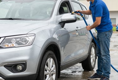 A friendly CleanPro smiling while cleaning a shiny car at a customer's doorstep in an urban Indian neighborhood.