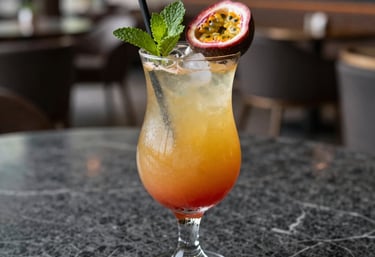 Still life photography of a colorful tropical cocktail with passion fruit and mint, set on a dark gray marble surface in a South American luxury lounge, soft natural light.