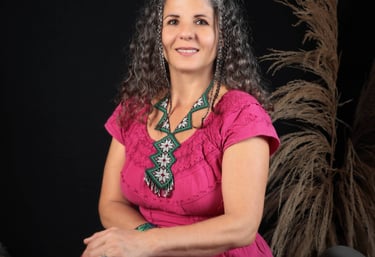 Zsofia, founder of Brevard Massage and Sound Therapy, in a pink folk dress seated by soft reeds