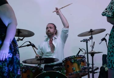 Professional male drummer playing an acoustic drum kit during a live musical performance.